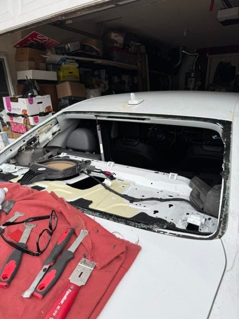 Auto glass tools laid out beside a vehicle with windshield removed showing exposed pinchweld