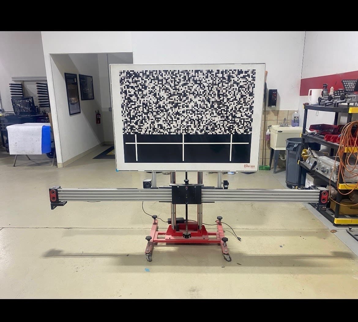 Windshield-mounted ADAS sensor module and wiring exposed during camera recalibration target stand while calibrating