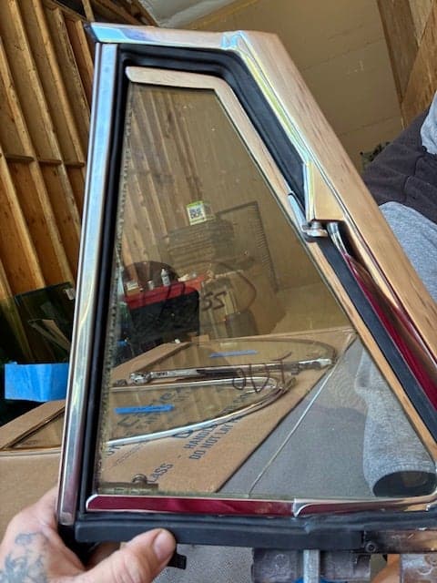 Restored chrome-framed classic car vent window glass held by a technician