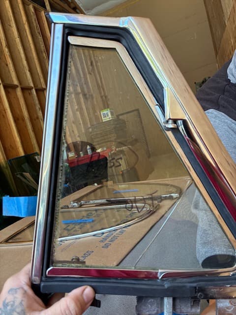 Restored chrome-framed classic car vent window glass held by a technician